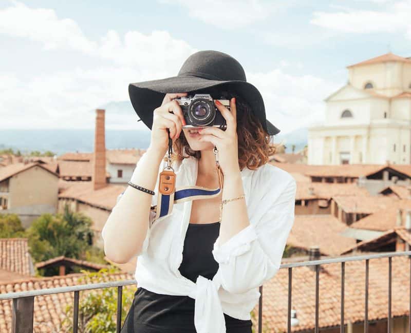 A woman with a camera up to her face points the camera at the viewer.|A yellow car drives through a landscape with canyons.|A man stands on a rocky ledge looking out at a waterfall.