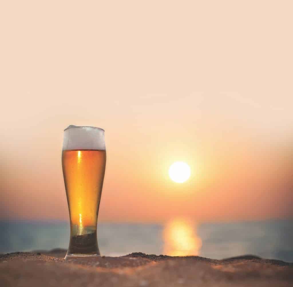 A beer on the beach during sunset.