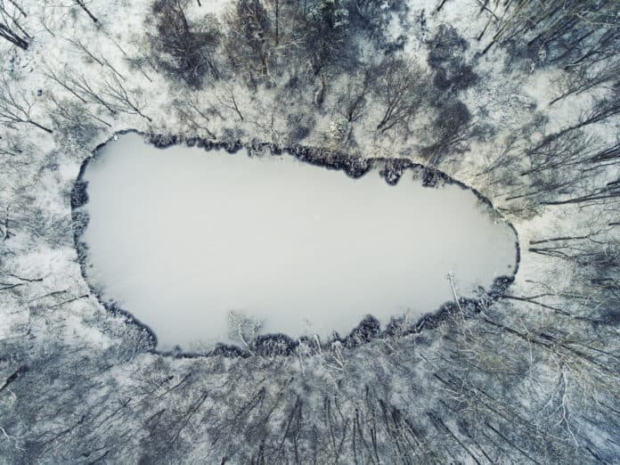 Aerial of frozen pond with first ice during Winter.