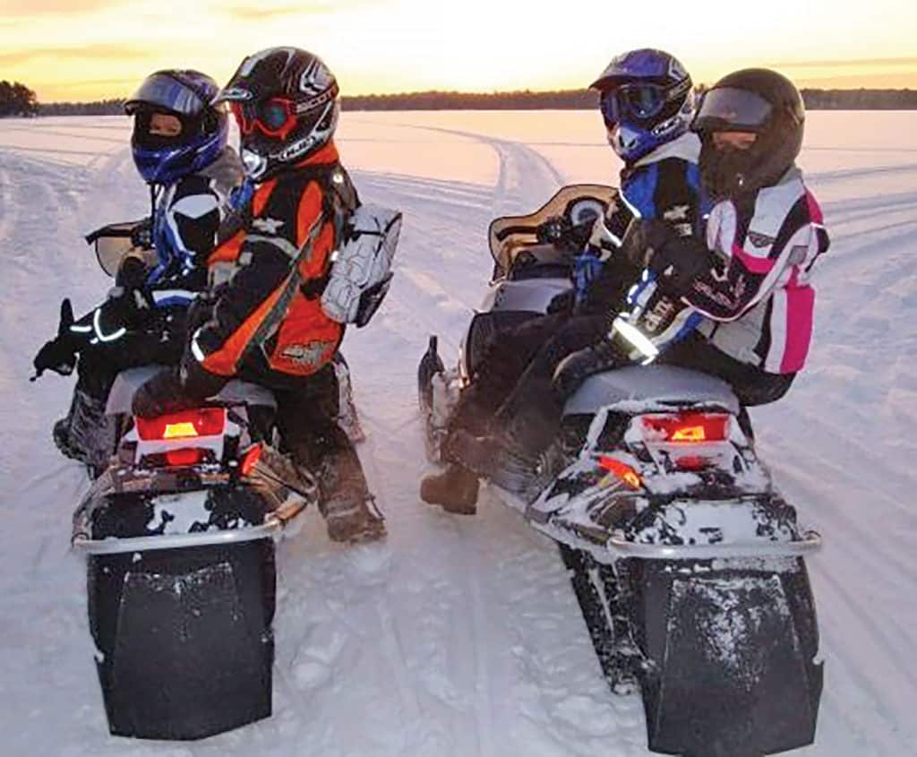 Two couples snowmobiling on a groomed trail. 