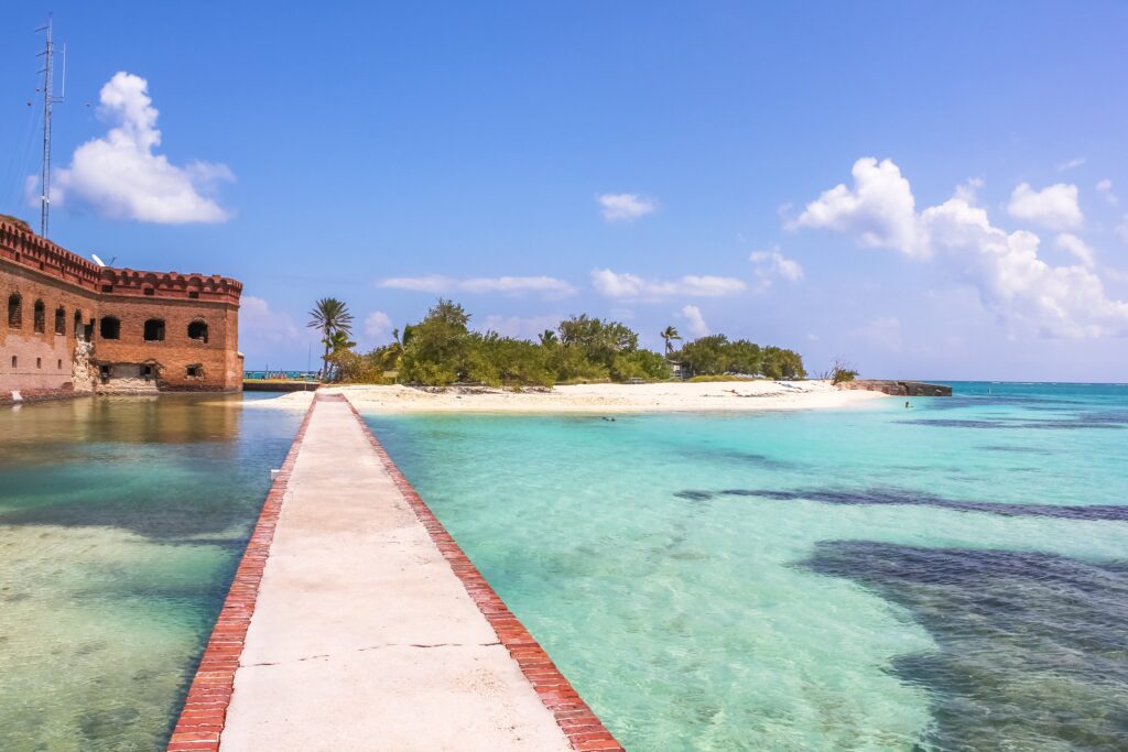 A stone boardwalk, turquoise waters and an island with the remnants of an old fort. 