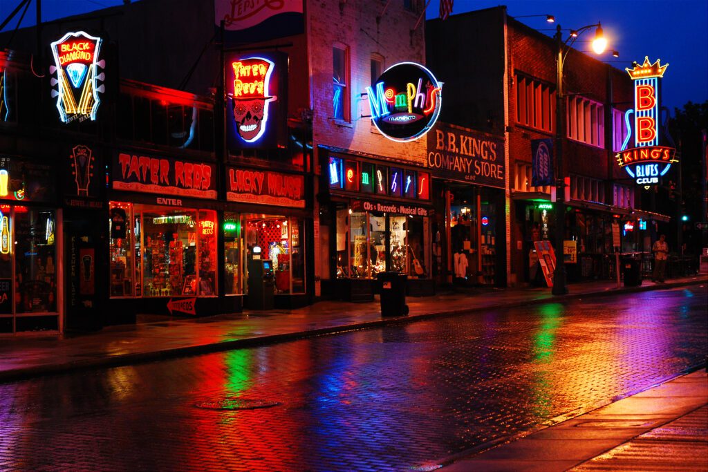 A vibrant, neon-lit street scene at night, showcasing various colorful signs for clubs and bars. The wet cobblestone street reflects the lights, adding a dynamic glow to the urban atmosphere.