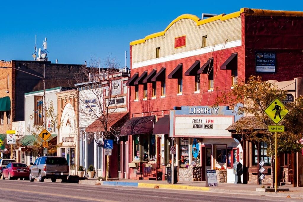 A small town street with colorful historic buildings. The red and white building in the center features a marquee sign for a theater called Liberty. Cars are parked along the street, and a pedestrian crossing sign is visible in the foreground.