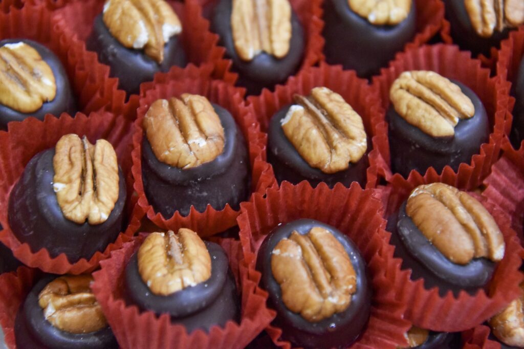 Assorted chocolate candies topped with pecan halves are arranged in red paper liners, creating a festive and inviting display.