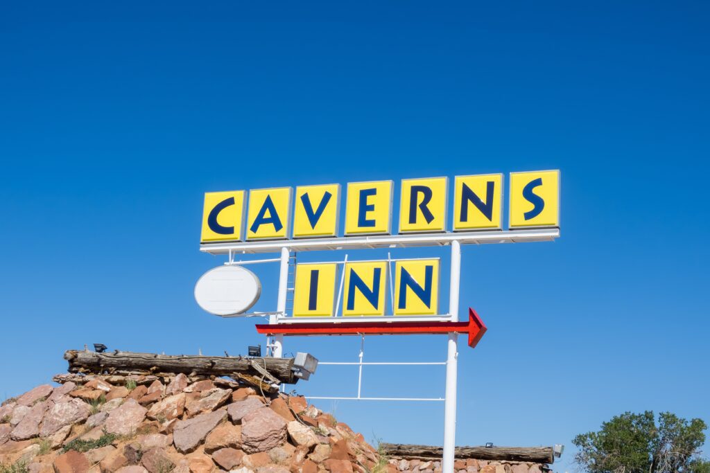 A retro yellow and blue sign reading CAVERNS INN stands above a rocky structure against a clear blue sky.