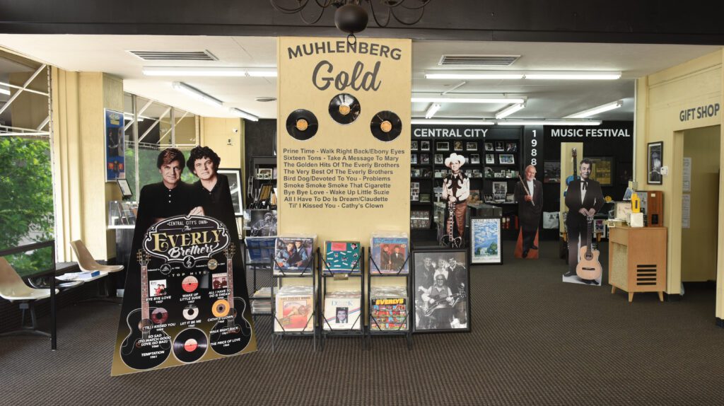 A museum display titled Muhlenberg Gold features vinyl records, posters, and memorabilia about the Everly Brothers and local music history. Cardboard cutouts, album covers, and music festival information are visible around the exhibit.