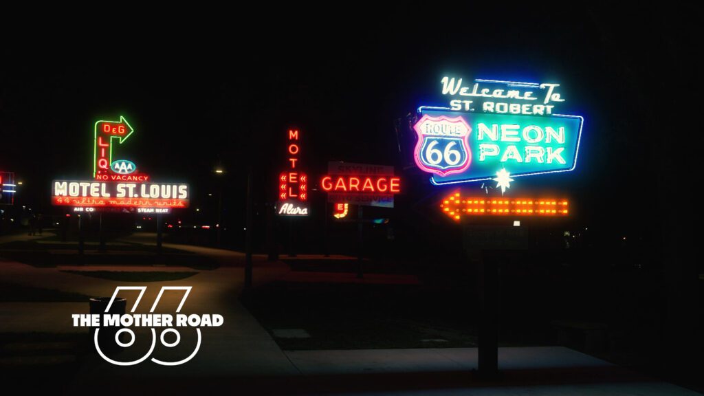 Neon signs at night display "Motel St. Louis," "Motel," "Garage," and "Welcome to St. Robert Route 66 Neon Park" along a sidewalk.