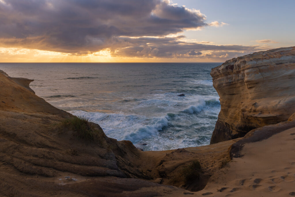 Coastal cliffs with ocean waves breaking below, under a partly cloudy sky at sunset.