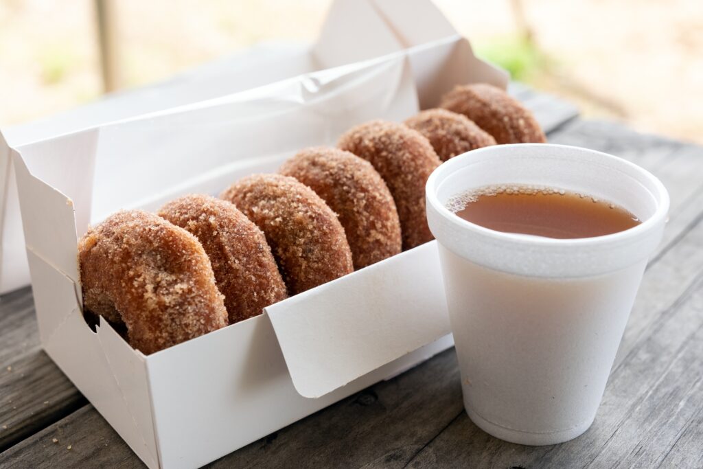 Five cinnamon sugar donuts in a white box next to a white foam cup filled with a brown liquid, on a wooden table.