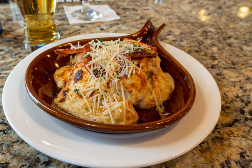 A brown dish with baked seafood topped with shredded cheese and herbs, served on a white plate on a granite countertop.