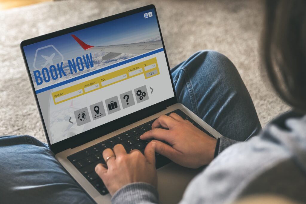 Person using a laptop to search for flights, with a “Book Now” banner and flight search fields displayed on the screen.
