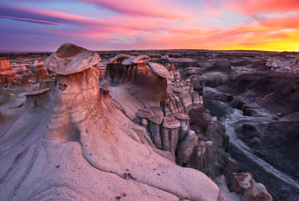 Eroded rock formations and hoodoos in a desert canyon landscape at sunset, with colorful clouds in the sky.