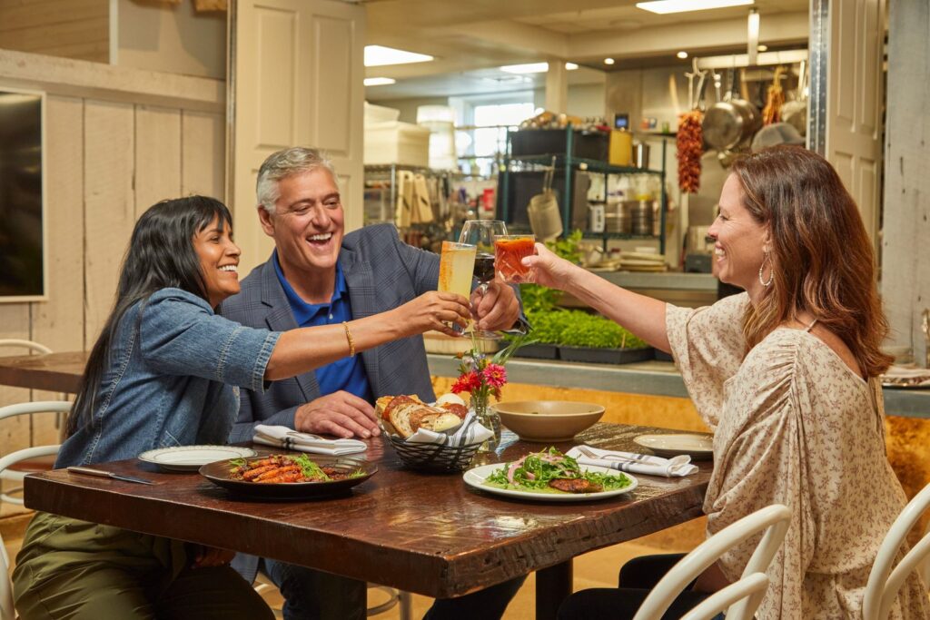 Three people at a restaurant table toasting with glasses of wine and cocktails.