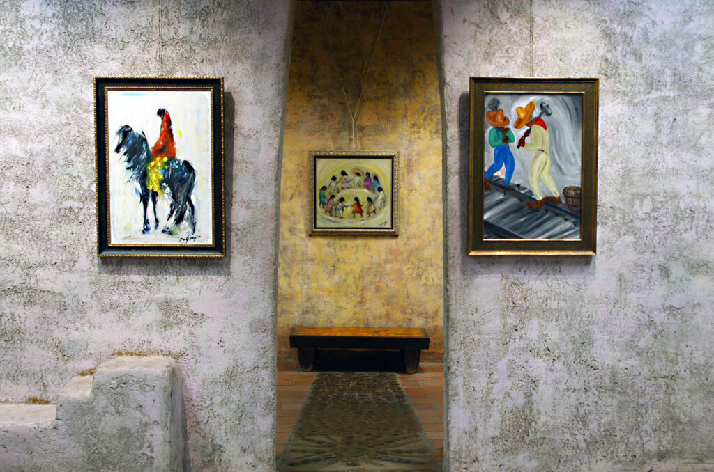 Three paintings displayed in an arched gallery space with a wooden bench in the background.