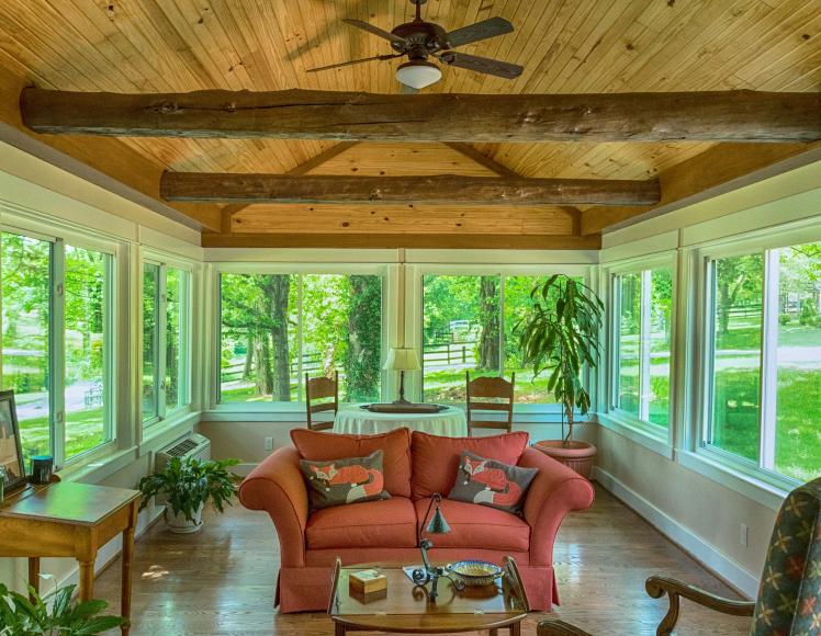 Sunroom with a wood-paneled ceiling, exposed beams, and a red sofa featuring fox-patterned throw pillows.