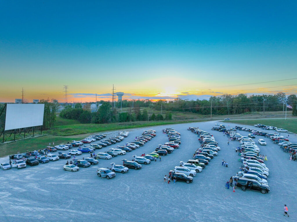 Cars parked in rows at an outdoor drive-in movie theater at sunset.