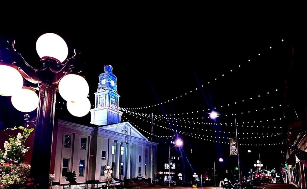 A historic white clock tower building illuminated at night, with strings of lights hanging over the street.