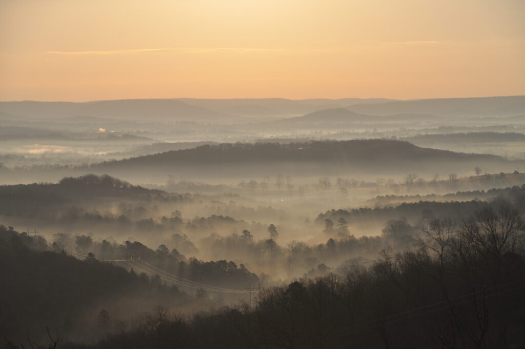 Layers of forested hills fading into fog under a pale sunset sky.