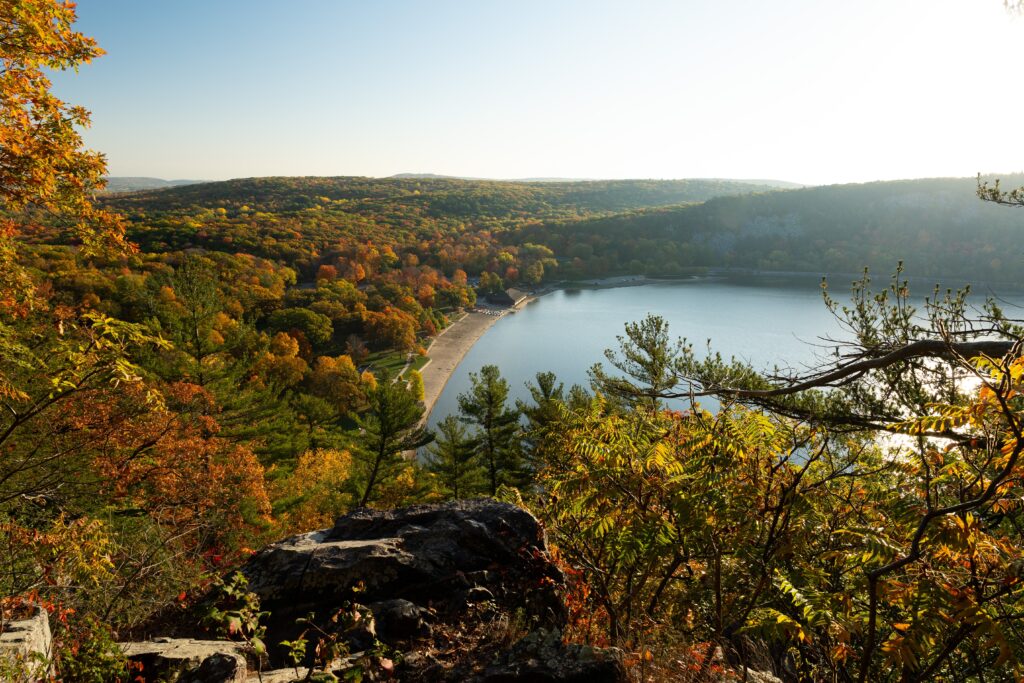 Elevated view of a lake bordered by a sandy beach and a forest with autumn foliage.
