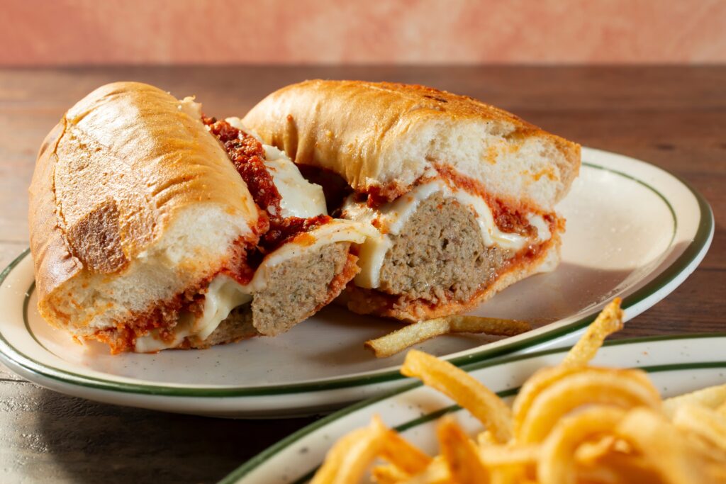 A meatball sub with melted cheese and marinara sauce on a plate, served with a side of fries.