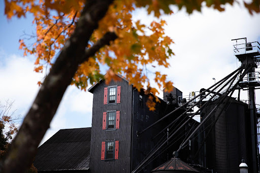 A black industrial building with red window shutters seen through orange autumn leaves.