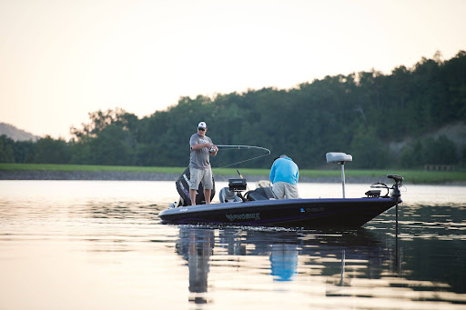 Two people fishing from a bass boat on a lake.