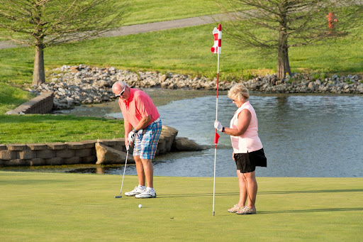 A man putting on a golf green while a woman stands nearby holding the flag.