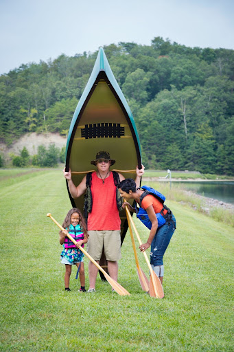 A family of three standing on a grassy hill with a canoe and paddles.
