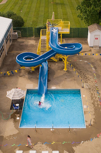 Aerial view of a blue spiral water slide emptying into a swimming pool with a person splashing at the bottom.